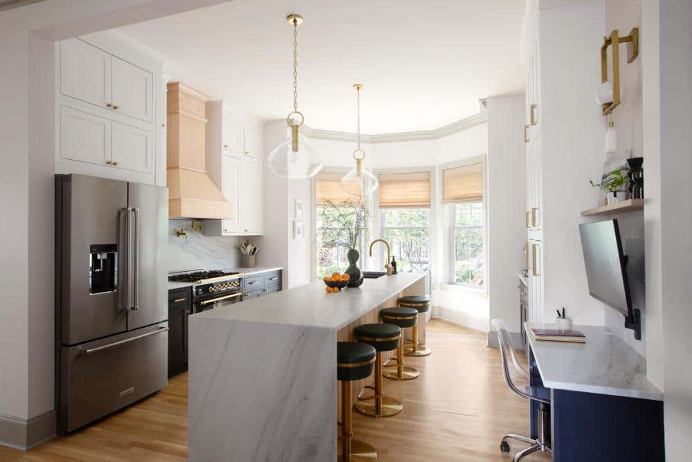 Stacked white inset kitchen cabinets with tall ceilings and navy blue inset shaker island with a waterfall creamy stone countertop