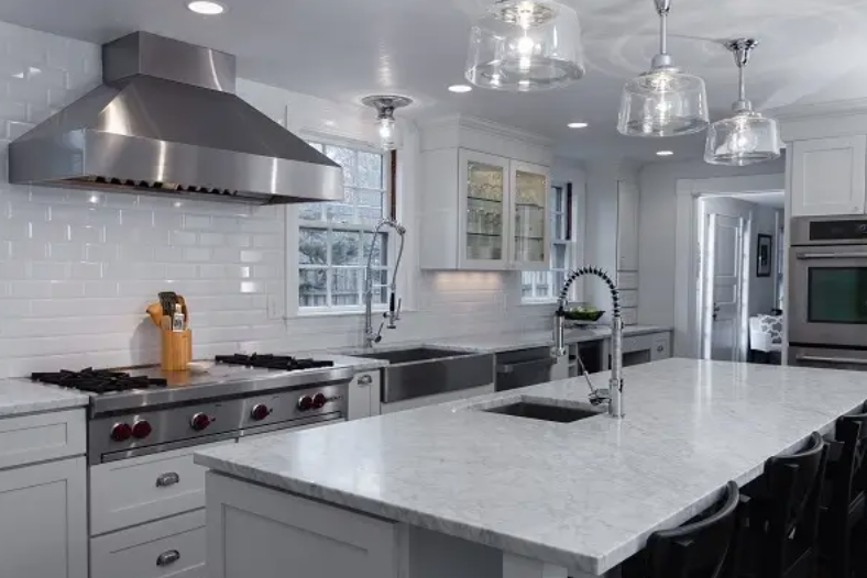 White shaker kitchen design with large stainless steel range hood above a built-in stainless steel gas cooktop