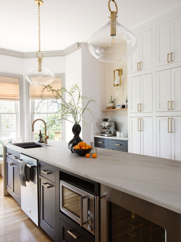 Stacked white inset shaker cabinets with black island cabinets, creamy waterfall countertops, funky glass and gold light fixtures, a natural wood kitchen hood