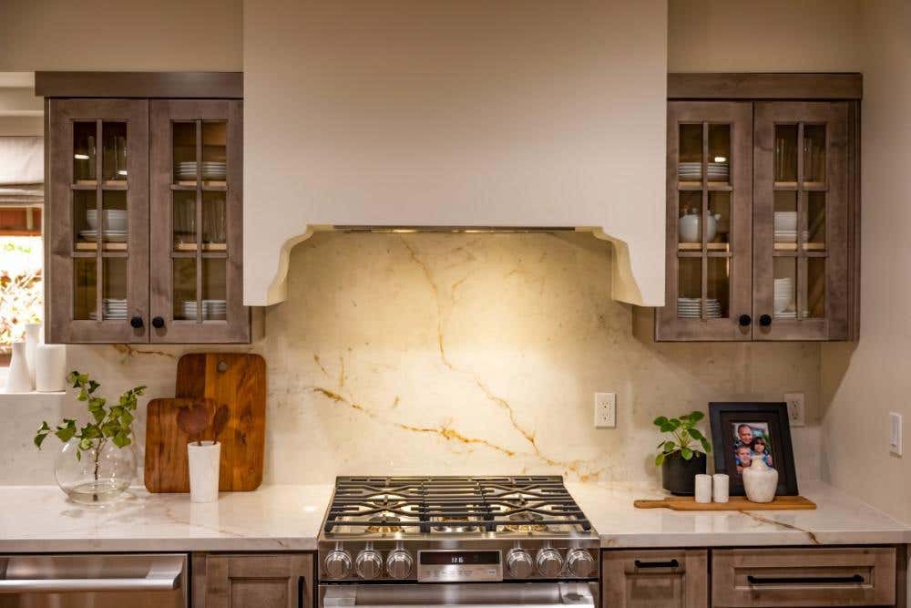 Mullion door rustic brown wall cabinets with a stone slab backsplash and rustic white range hood Mullion door rustic brown wall cabinets with a stone slab backsplash and rustic white range hood