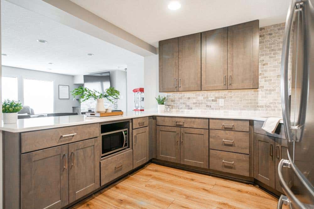 Medium-brown stained kitchen cabinets with mixed neutral stone backsplash and white countertops