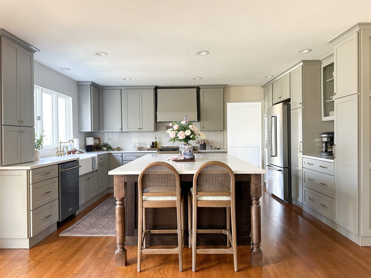 Light gray shaker kitchen cabinets with matching wood hood and dark brown stained island with decorative legs and marble-like quartz countertops