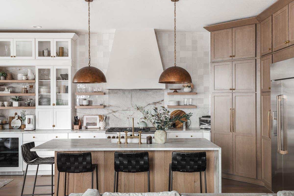 White and light wood kitchen design with an elegant tapered kitchen hood, gold cabinet hardware, and wood paneled island with half-waterfall countertop design.