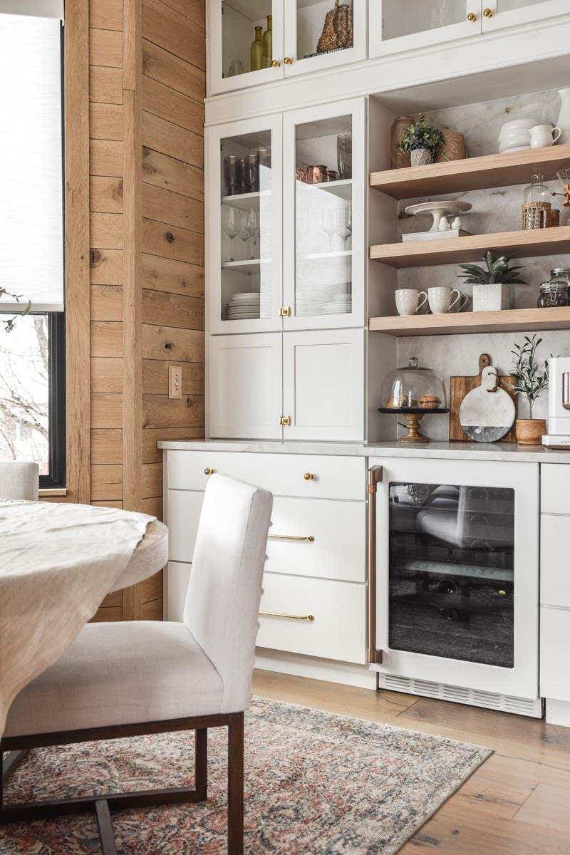 White shaker kitchen cabinets in a buffet design with stacked cabinets, gold hardware, and floating wood shelves in the center.