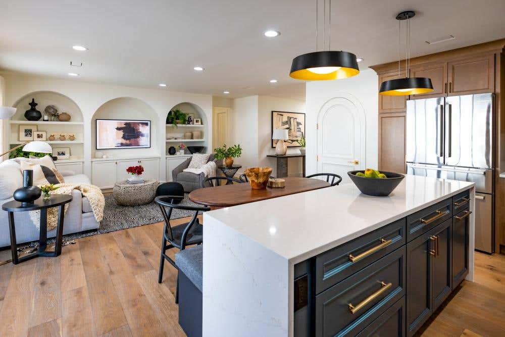 Light wood U-shaped kitchen design with wood floating shelves and an indigo island with white quartz waterfall countertop