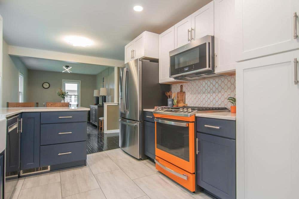 Shaker kitchen design with a peninsula with white wall cabinets, blue base cabinets and a bright orange gas range Shaker kitchen design with a peninsula with white wall cabinets, blue base cabinets and a bright orange gas range
