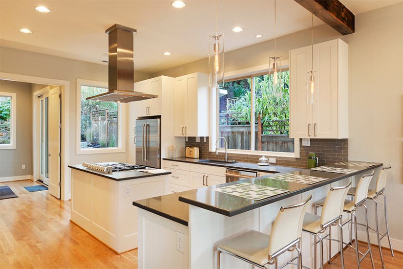 White L-shaped shaker kitchen design with a center island and stainless steel island range hood