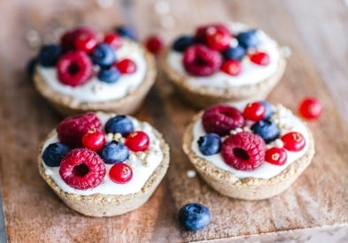 Four fruit tarts with raspberries, blueberries, and cream.