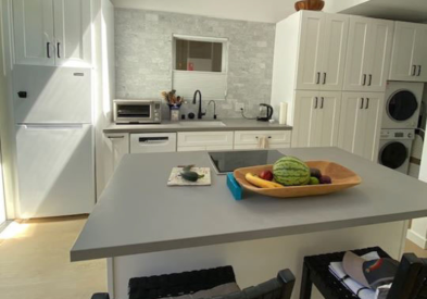 Contemporary one-wall white shaker kitchen and island with integrated stacked laundry machines and medium gray modern quartz countertops