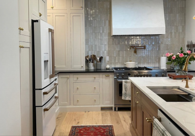 Cream colored inset shaker kitchen cabinets with warm wood-toned island, tan quartz countertops and textured glazed tile backsplash behind a tapered kitchen hood