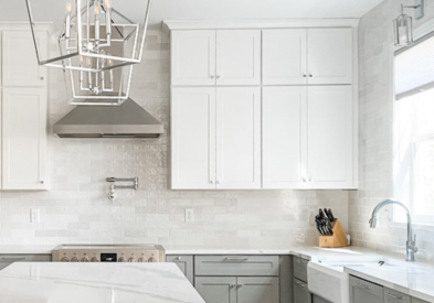 White and light gray shaker kitchen cabinets with white quartz waterfall countertops and polished chrome light fixtures