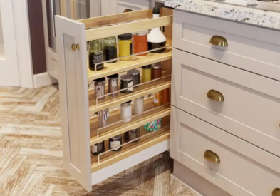 White shaker kitchen cabinets with gold cup pulls and a pull-out storage cabinet holding spices and oils