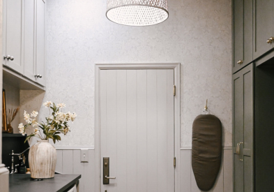 Large laundry room with washer/dryer on left with taupe shaker cabinets above and decorative black countertop across with olive green mudroom lockers and white oak bench on the right