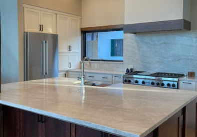 Large white shaker kitchen with a large dark brown wood island and creamy stone countertops