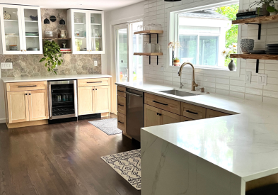 Scandinavian and Bohemian kitchen design with white shaker wall cabients and natural wood shaker base cabinets with black hardware, white quartz countertops, woven light fixtures and wood floating shelves