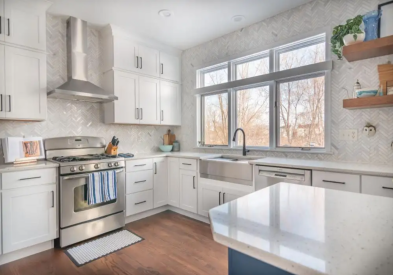 White shaker kitchen with stacked cabinets, black cabinet hardware, a full tile backsplash up to the ceiling and a blue shaker island