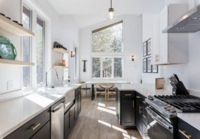 polished kitchen with black and white cabinets opens to a dining room with a large window stretching to the ceiling