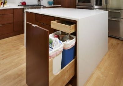 A Wastebasket cabinet in CliqStudios Studio 31 style in Cider finish containing a full trash can and full recycling bin.