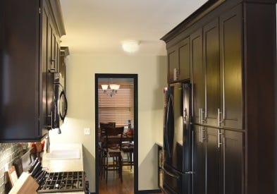 pantry wall in galley kitchen is built with dark birch cabinets, stacked crown molding, two tall pantry cabinets and a refrigerator cabinet