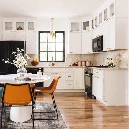 white kitchen with black appliances opens to dining area with white table and burnt orange chairs