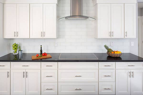 Modern white shaker style kitchen with curved stainless steel range hood, fruit, and wine