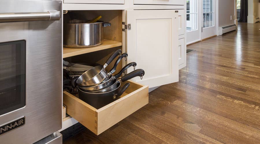Lower roll-out tray in a base cabinet storing stacked pots. and pans.