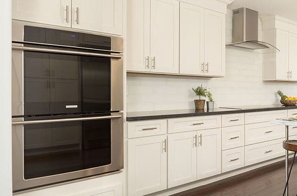 kitchen has double wall ovens in white shaker cabinets and glass cooktop on black granite countertop below glass range hood