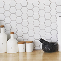 White honeycomb tile backsplash with decorative jars and a mortar in front.