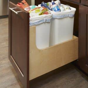 Pull-out waste cabinet with two trash bins inside of a dark wood-stained shaker cabinet