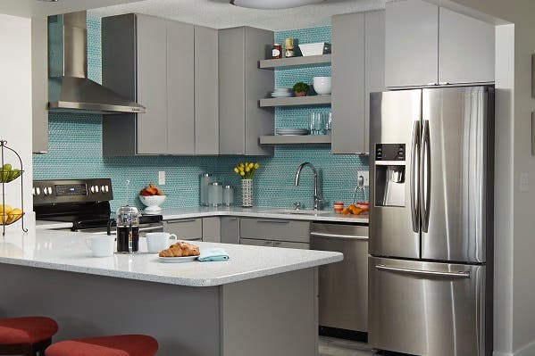 corner view of condo kitchen with gray slab door cabinets, ceiling high aqua glass mosaic tiles, stainless range hood and floating shelves corner view of condo kitchen with gray slab door cabinets, ceiling high aqua glass mosaic tiles, stainless range hood and floating shelves
