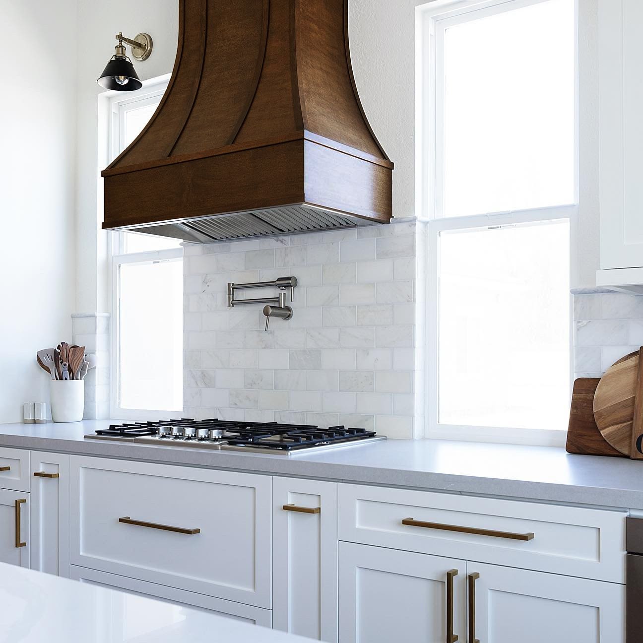 Curved wood range hood with wood strapping in warm brown stain against white shaker cabinets