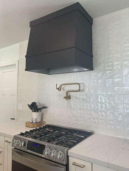 Angled wood range hood in black against white subway tile wall with white shaker base cabinets Angled wood range hood in black against white subway tile wall with white shaker base cabinets