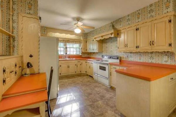 outdated kitchen with flower wallpaper, yellowed cabinets and orange countertops