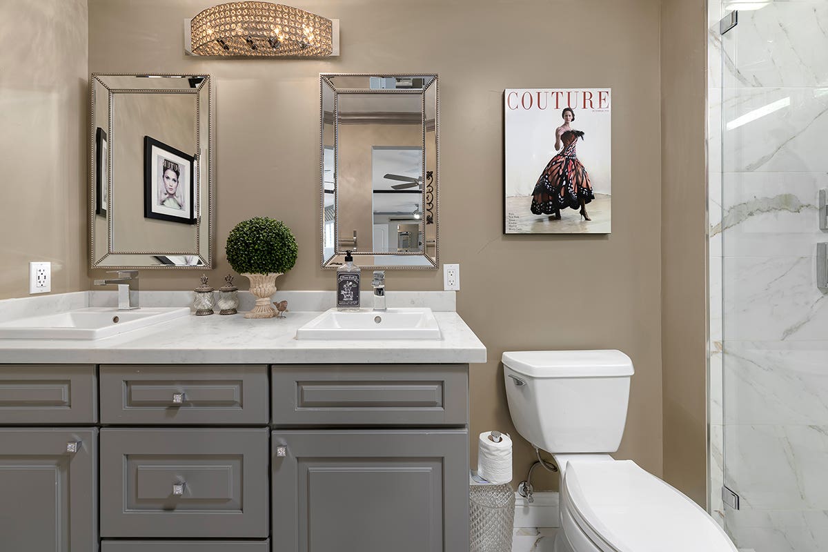 Charcoal gray raised panel bathroom vanity with chrome knobs, white square porcelain sinks, and white solid surface countertops