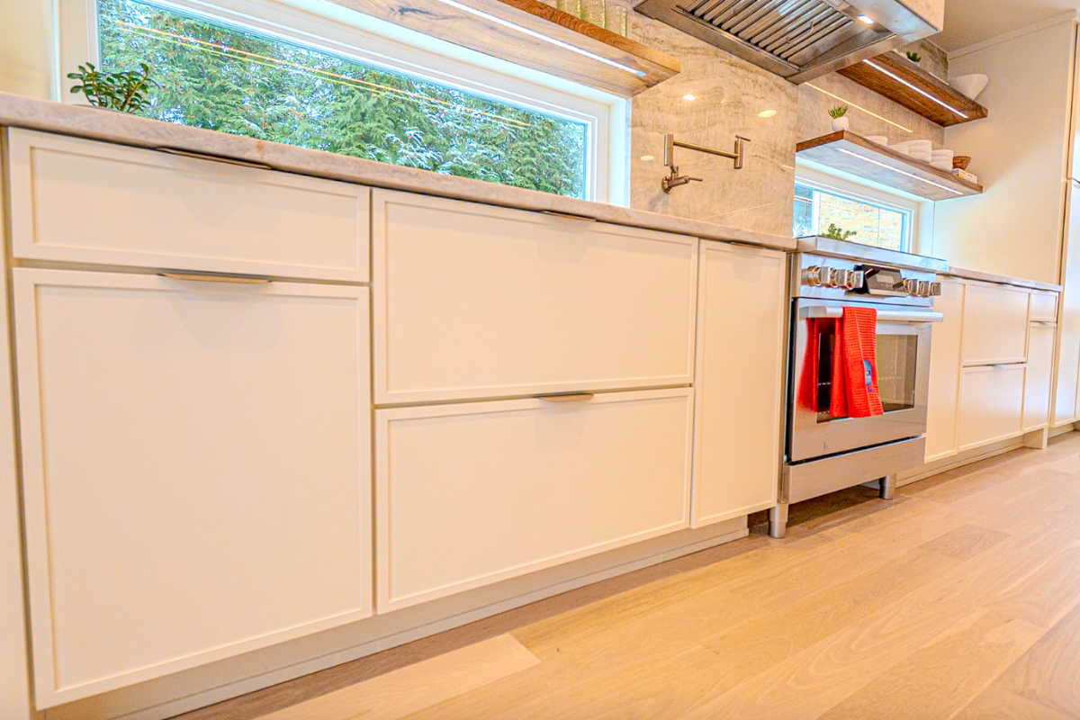 Cream-colored skinny shaker kitchen design with a large island, brass finger pulls and warm quartzite countertops