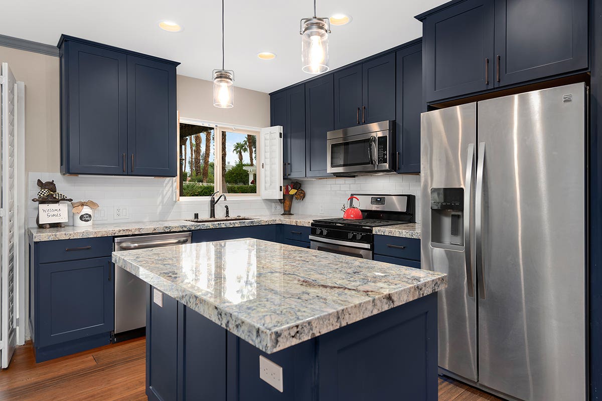 L-shaped blue painted shaker kitchen cabinets with island and gold, cream, and blue granite countertops L-shaped blue painted shaker kitchen cabinets with island and gold, cream, and blue granite countertops