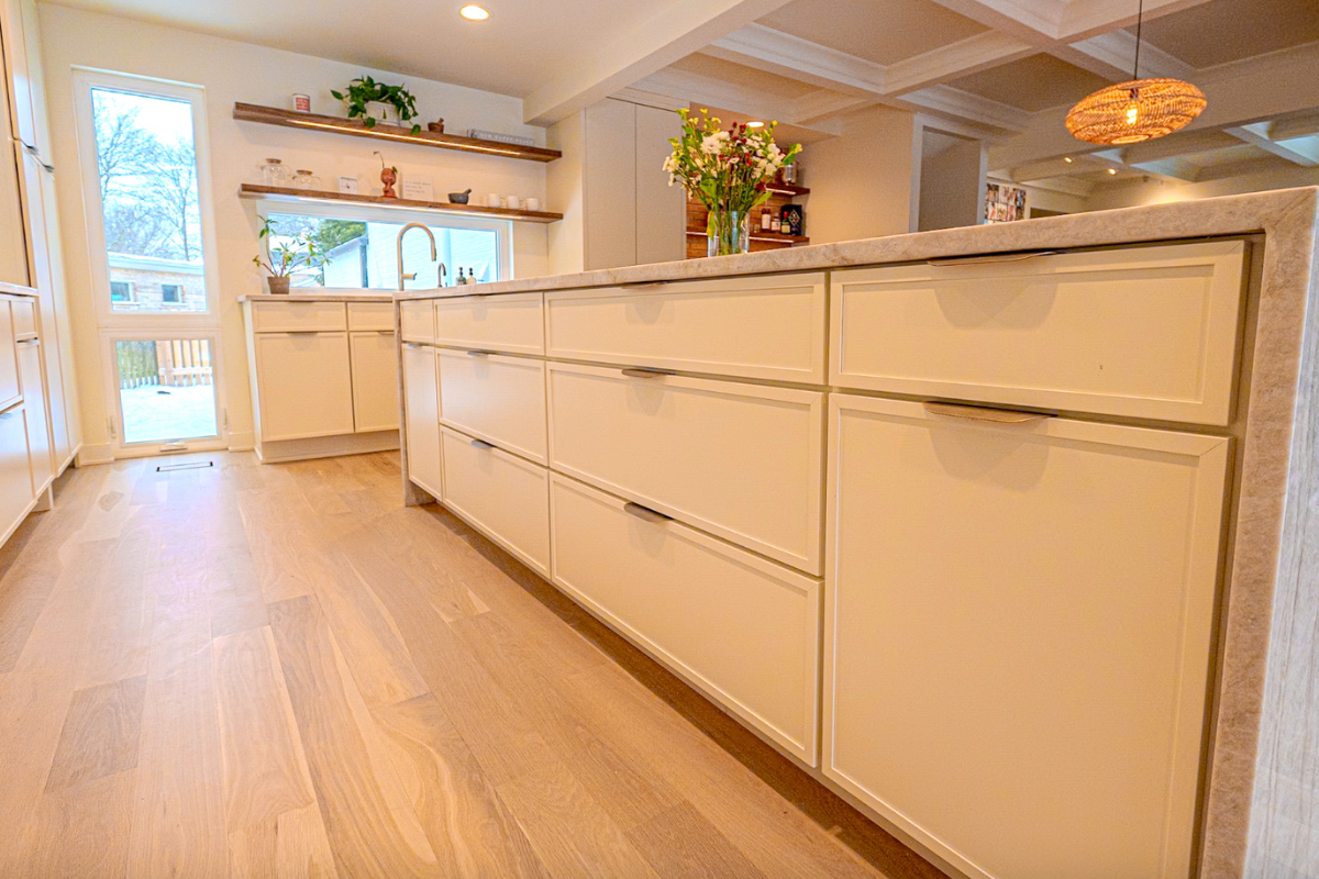 Cream-colored skinny shaker kitchen design with a large island, brass finger pulls and warm quartzite countertops