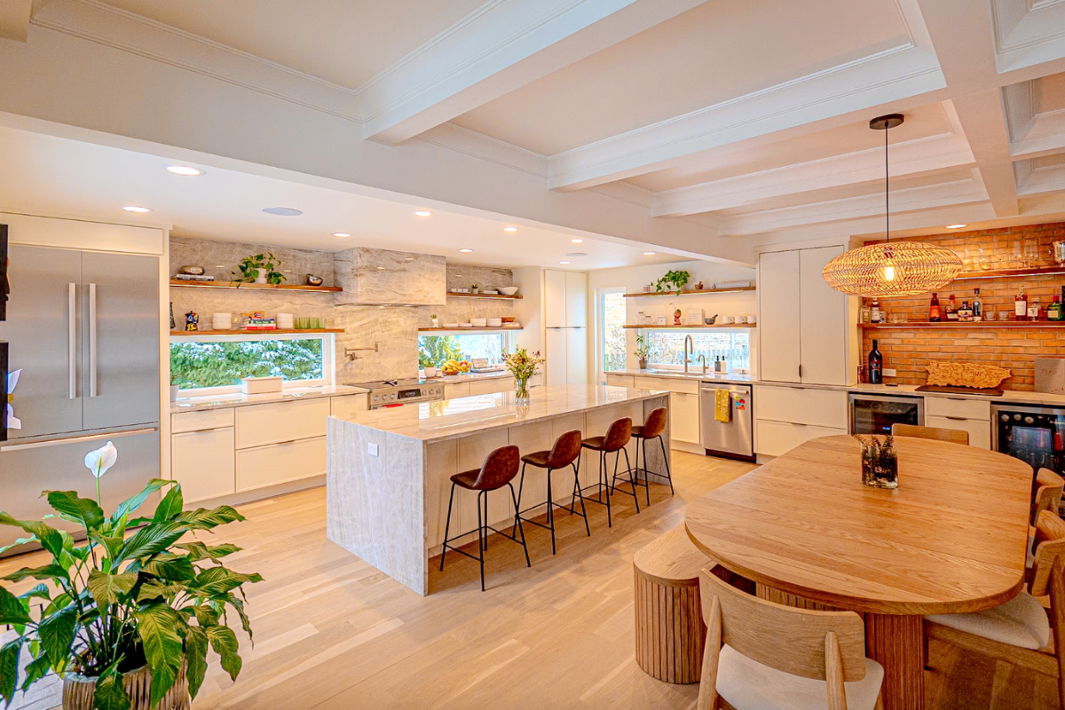 Cream-colored skinny shaker kitchen design with a large island, brass finger pulls and warm quartzite countertops
