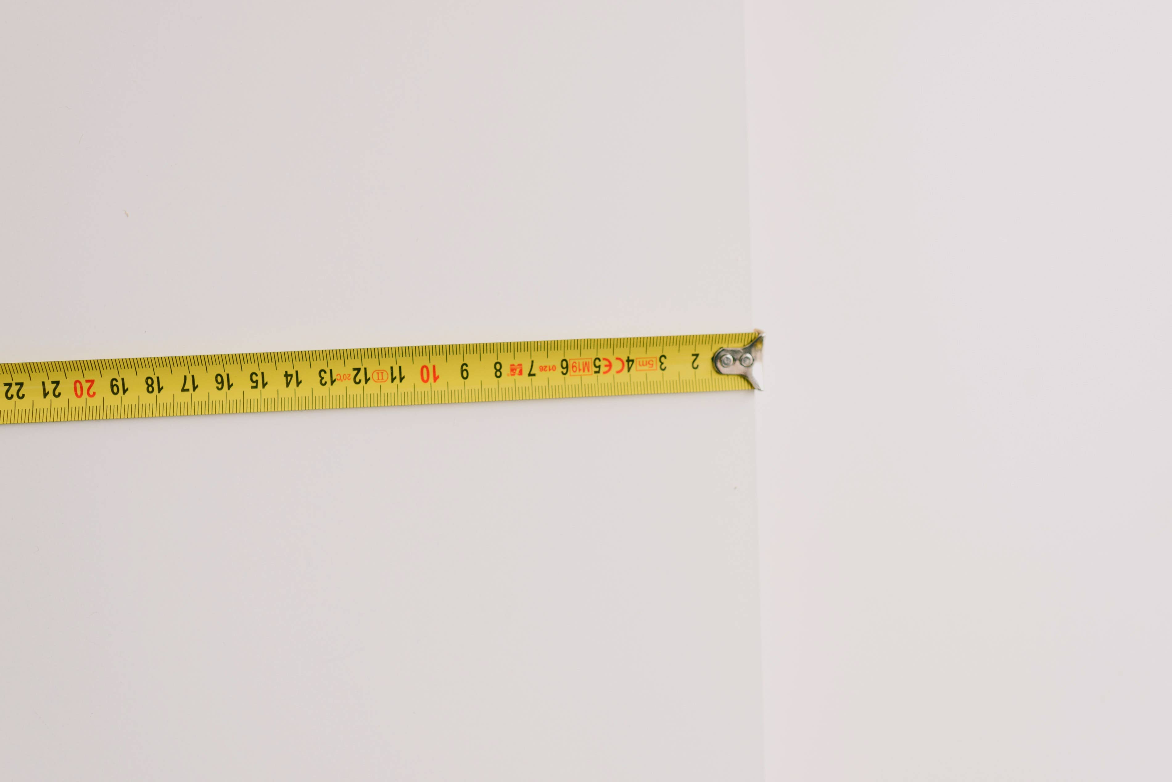 Person using tape measure to measure the length of a wall Person using tape measure to measure the length of a wall