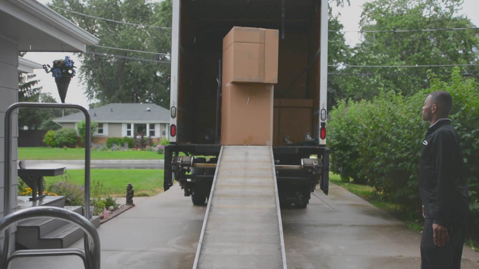 Delivery driver in black clothing waiting at end of trucks ramp for assistant to wheel down cabinet boxes Delivery driver in black clothing waiting at end of trucks ramp for assistant to wheel down cabinet boxes