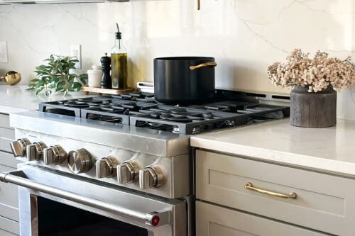 Duluth Pebble kitchen cabinets Close-up of a stunning gas chef’s range next to beige kitchen cabinets with shaker door style and brass cabinet hardware
