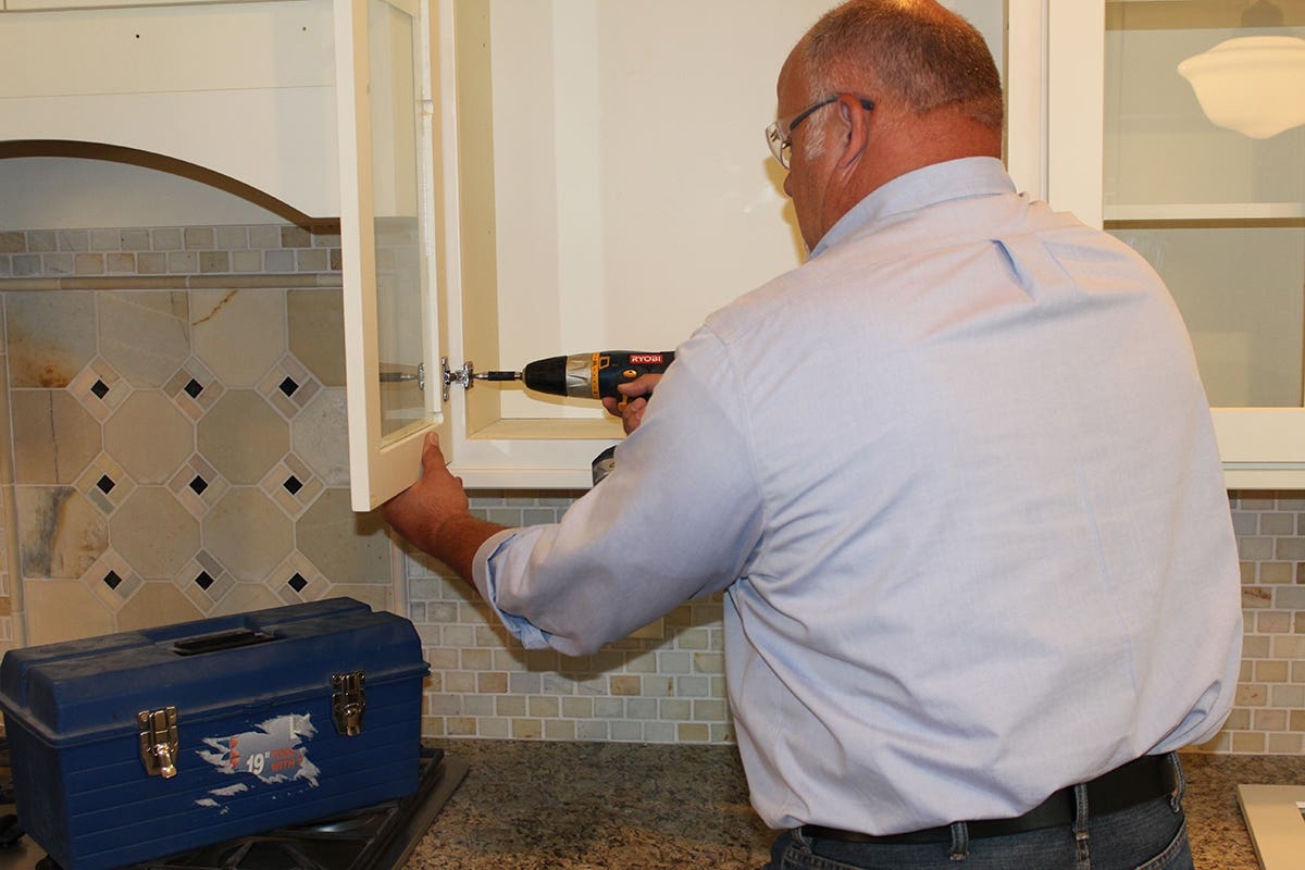 Homeowner with rimmed glasses using power drill to adjust glass cabinet door