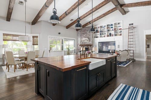 Large open kitchen and living room layout Large open kitchen and living room layout with black shaker island with butcher block countertops and a built-in white shaker entertainment center in the background with open cabinet storage above