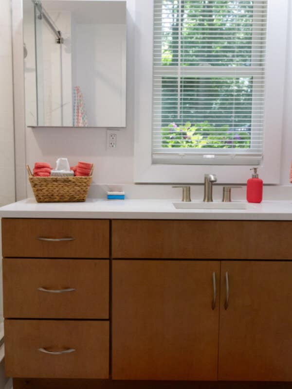 Medium wood tone vanity cabinet in slab door style with white countertops Medium wood tone vanity cabinet in slab door style