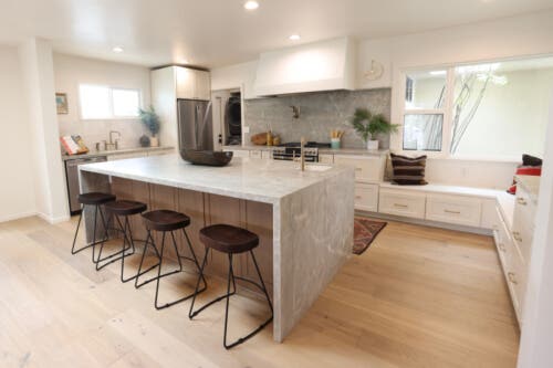 Newport Silk and Fossil kitchen cabinets U-shaped shaker kitchen with cream cabinets in Mid-Century Modern style with large plaster range hood and medium wood-toned island with gray waterfall countertops