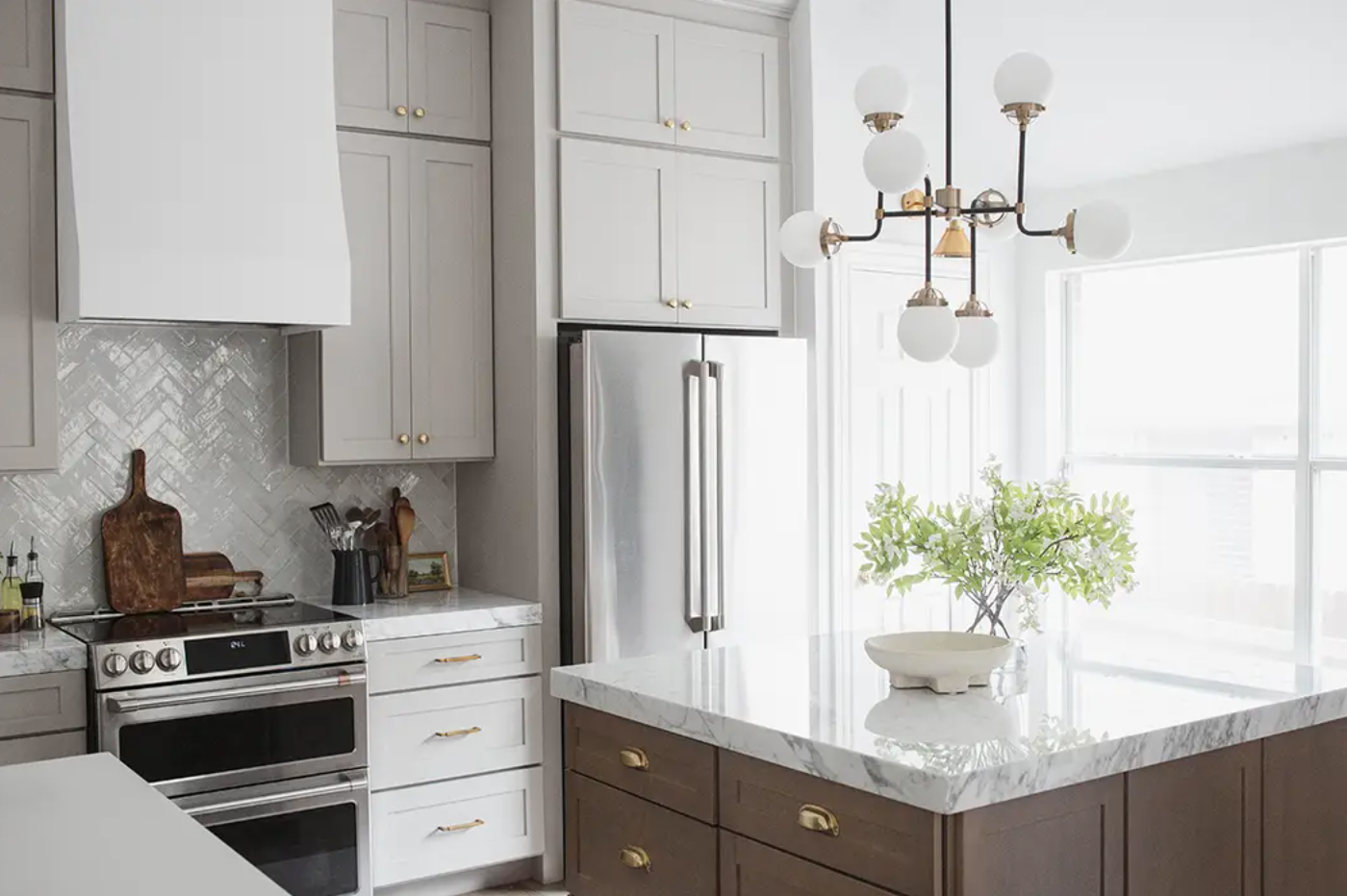 Light gray and medium wood stained kitchen cabinets with an island, marble countertops, and brass fixtures.