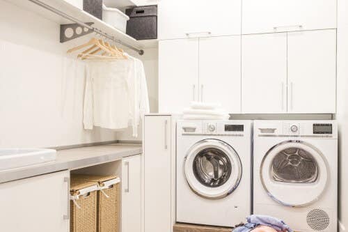 White slab laundry room design with hanging rod above countertops White slab laundry room design with hanging rod above countertops