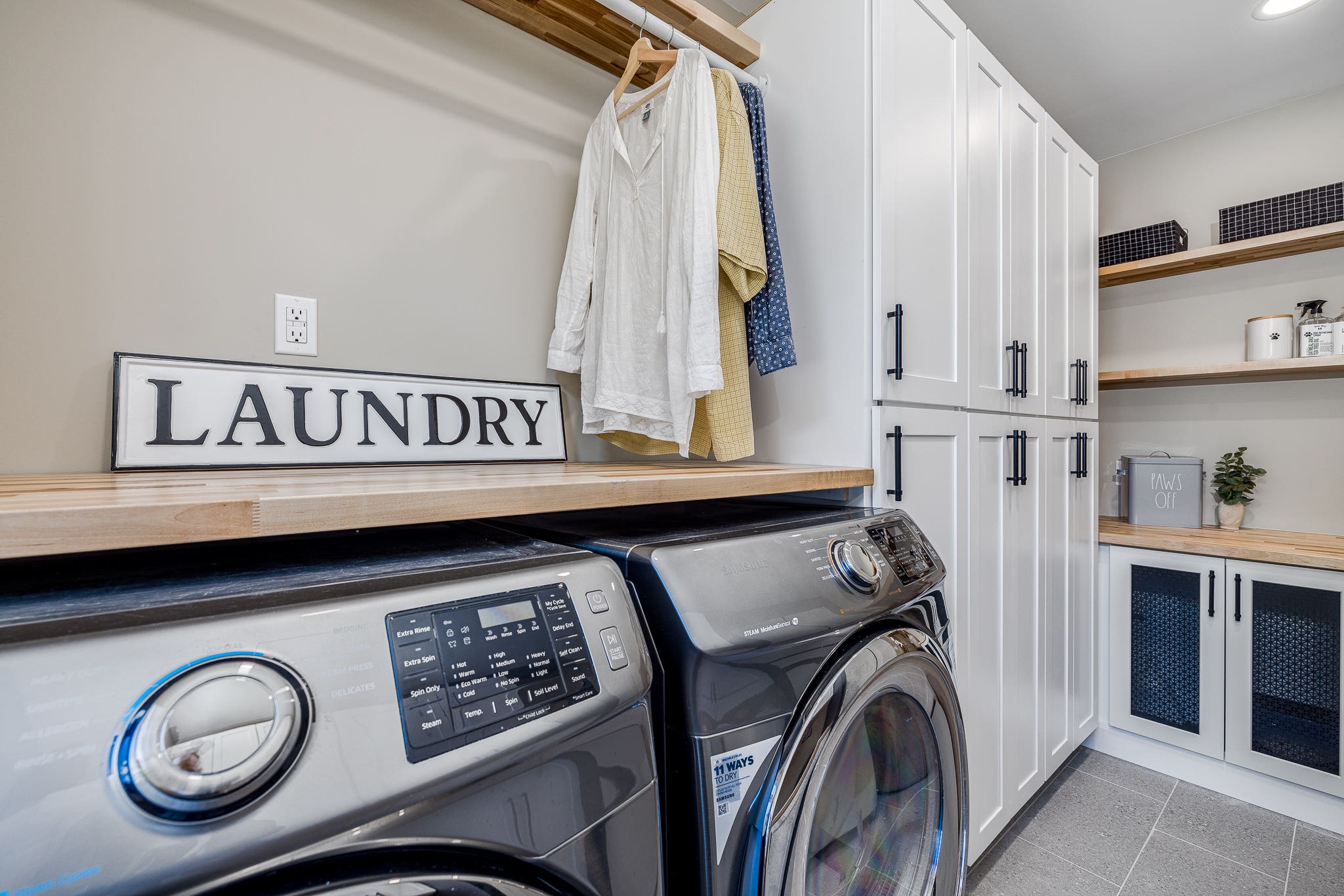 CliqStudios project: Shaker white laundry room sink cabinets with black hardware pulls and light butcher block countertops