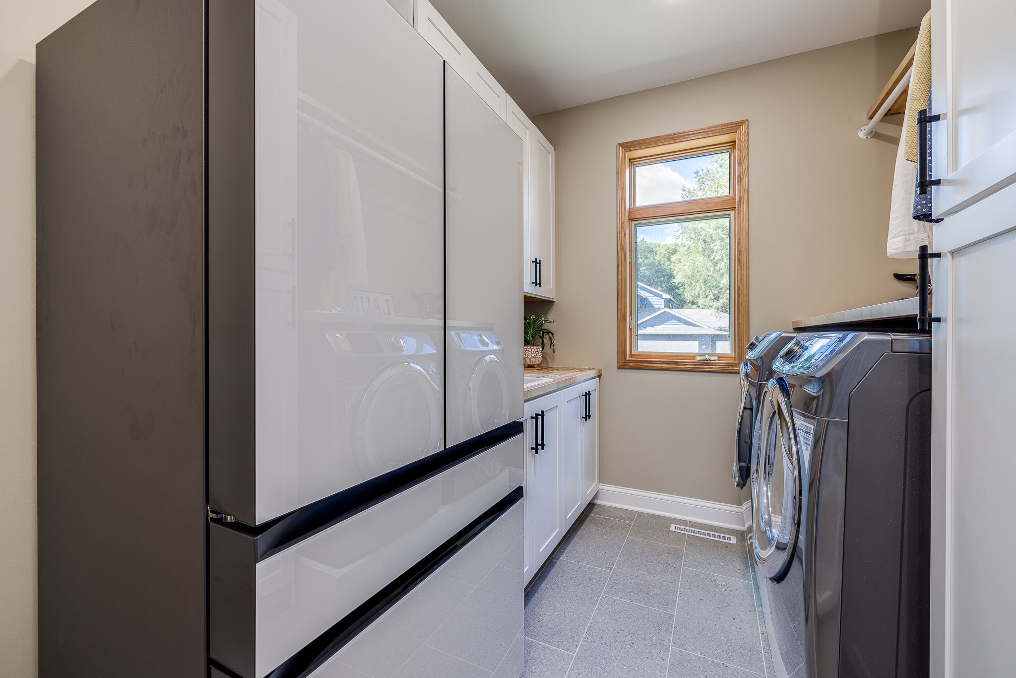 CliqStudios project: Shaker white laundry room sink cabinets with black hardware pulls and light butcher block countertops