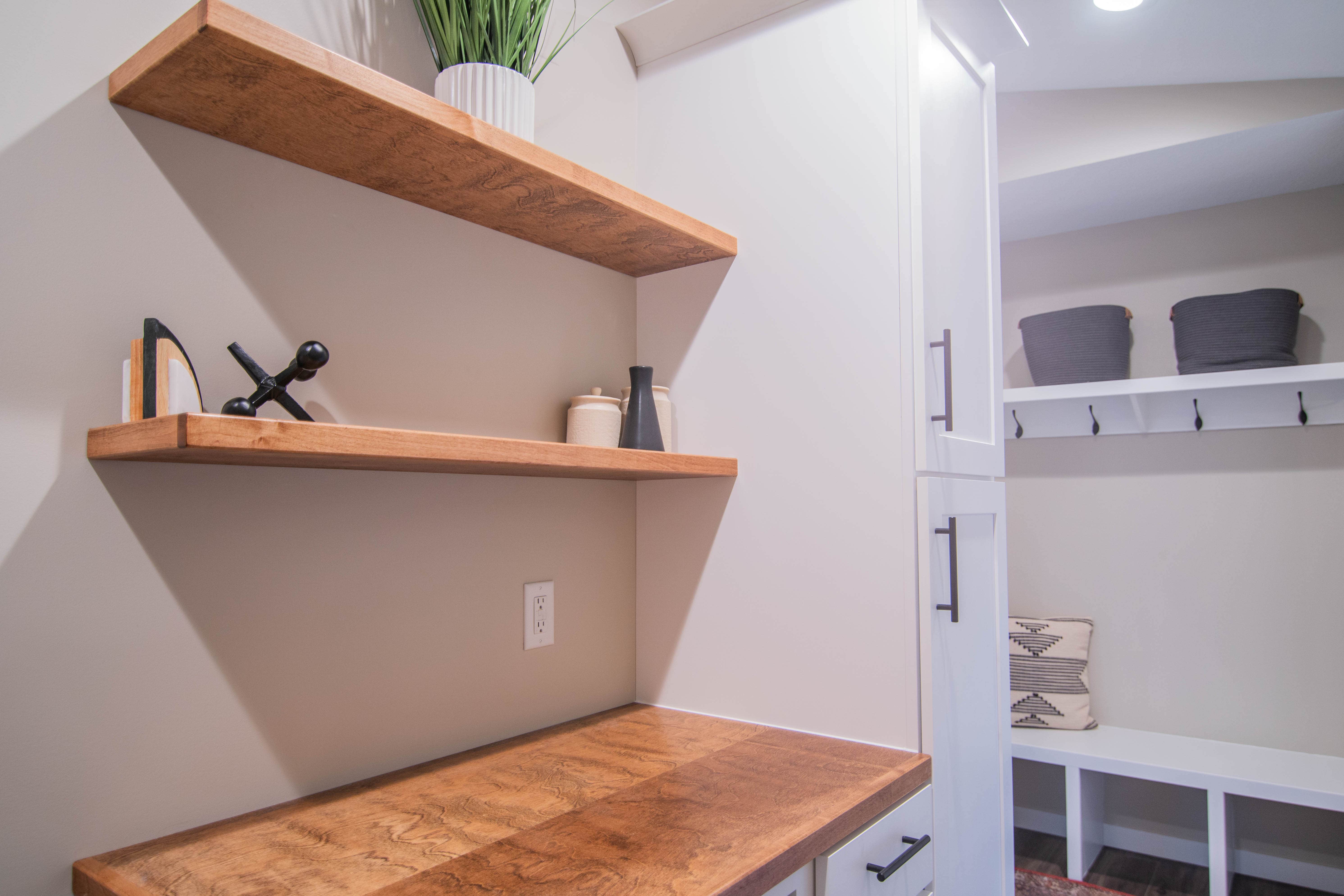 CliqStudios project: White laundry and mudroom cabinets with warm golden wood floating shelves and a mudroom bench